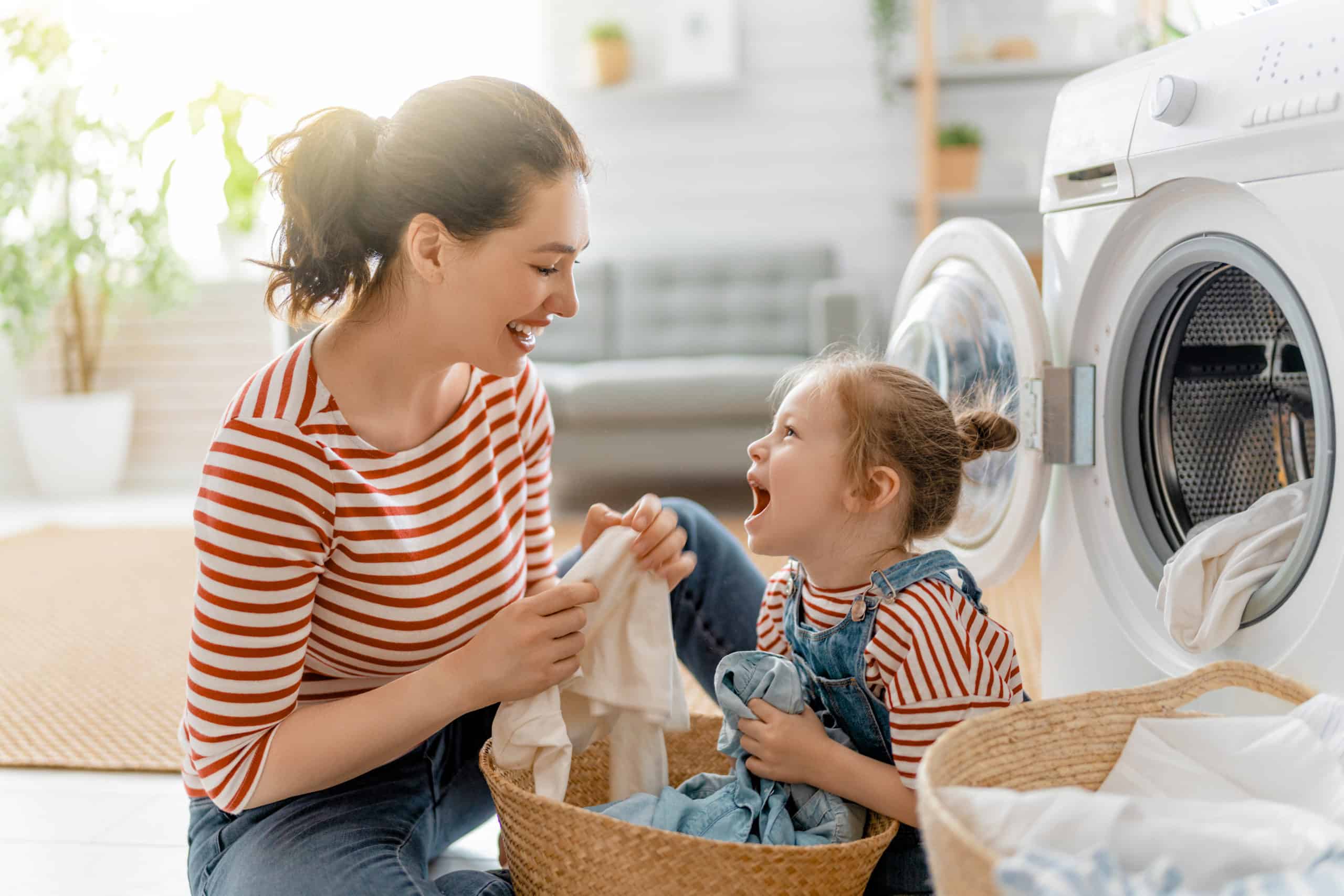 A picture of a young woman and her daughter smiling and folding clothes outside their dryer.