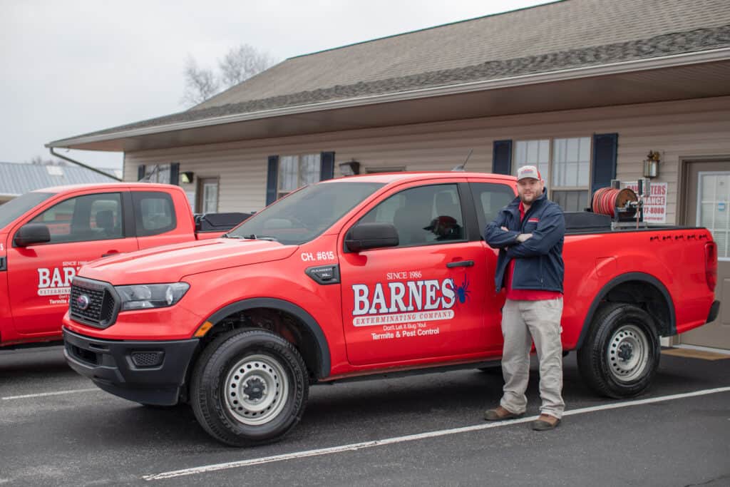 Image of a man standing, with his arms crossed, outside the newer Barnes exterminating trucks.