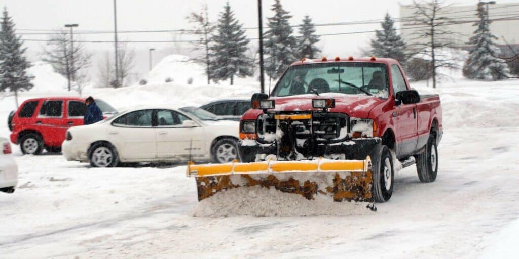 A picture of a red truck shoveling snow with a snow plow.